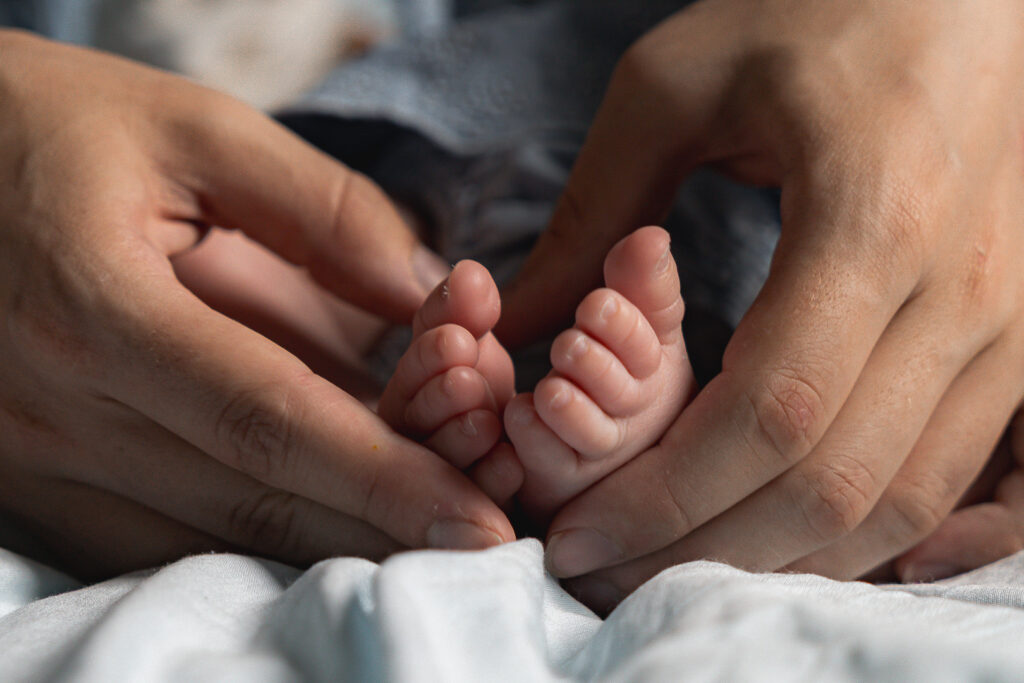 Détails des pieds d'un bébé nouveau-né tenus par les mains de maman lors d'une séance naissance lifestyle à domicile à Blanquefort