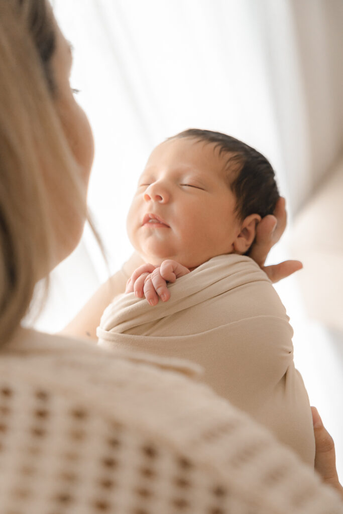 Bébé nouveau-né emmailloté tenu par sa maman lors d'une séance naissance à mon home studio sur Bordeaux