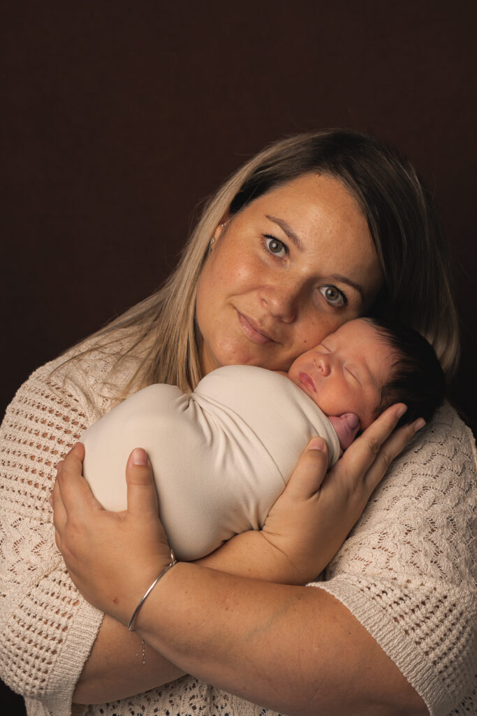 Bébé nouveau-né emmailloté en baby-posing dans les bras de sa maman joue contre joue lors d'une séance naissance à mon home studio de Bordeaux