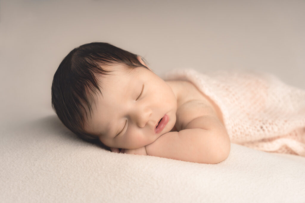 Bébé nouveau-né qui dort la tête posée sur ses mains lors d'une séance naissance en baby-posing à mon home studio sur Bordeaux