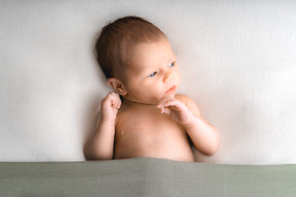Bébé nouveau-né nu en baby posing qui regarde sur le côté lors d'une séance naissance à mon home studio sur Bordeaux