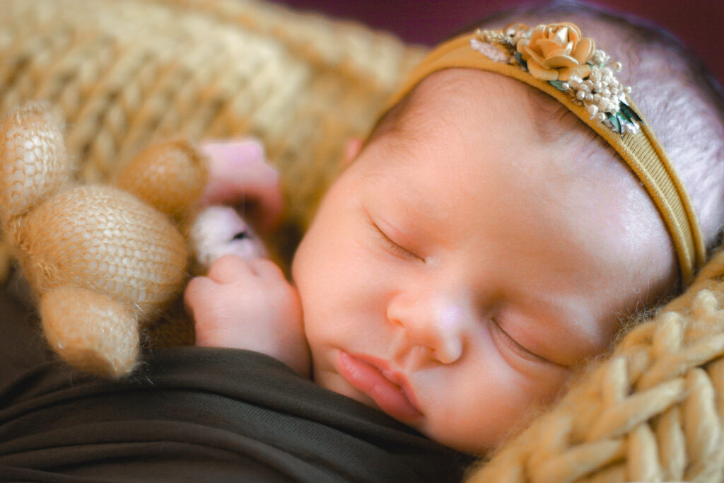 Gros plan sur un bébé nouveau-né en baby posing qui dort en tenant un nounours lors d'une séance naissance à mon home studio sur Bordeaux