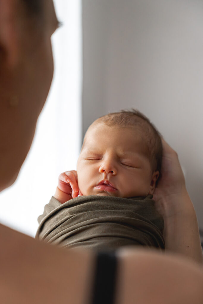 Bébé nouveau-né emmailloté dans un tissu kaki lors d'une séance naissance en home studio à Bordeaux