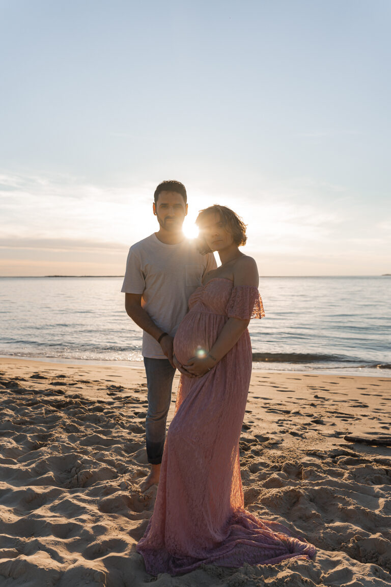 Couple sur la plage, devant la mer au coucher du soleil durant leur séance photo grossesse en extérieur aux dunes du pilat sur le bassin d'Arcachon