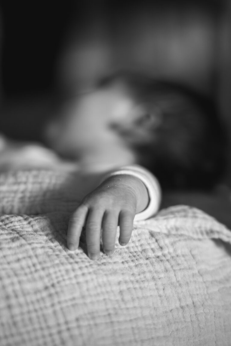 Détail en noir et blanc d'une main d'un bébé qui dort lors d'une séance naissance au home studio à Bordeaux