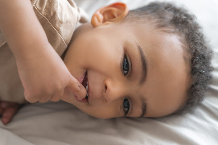 Portrait d'un petit garçon allongé sur son lit, les doigts à la bouche, le regard rêveur lors d'une séance photo à domicile à Pessac