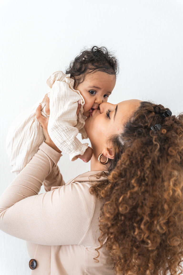 Bébé tenu par sa maman qui l'embrasse sur la bouche lors d'un shooting bébé à domicile à Pessac