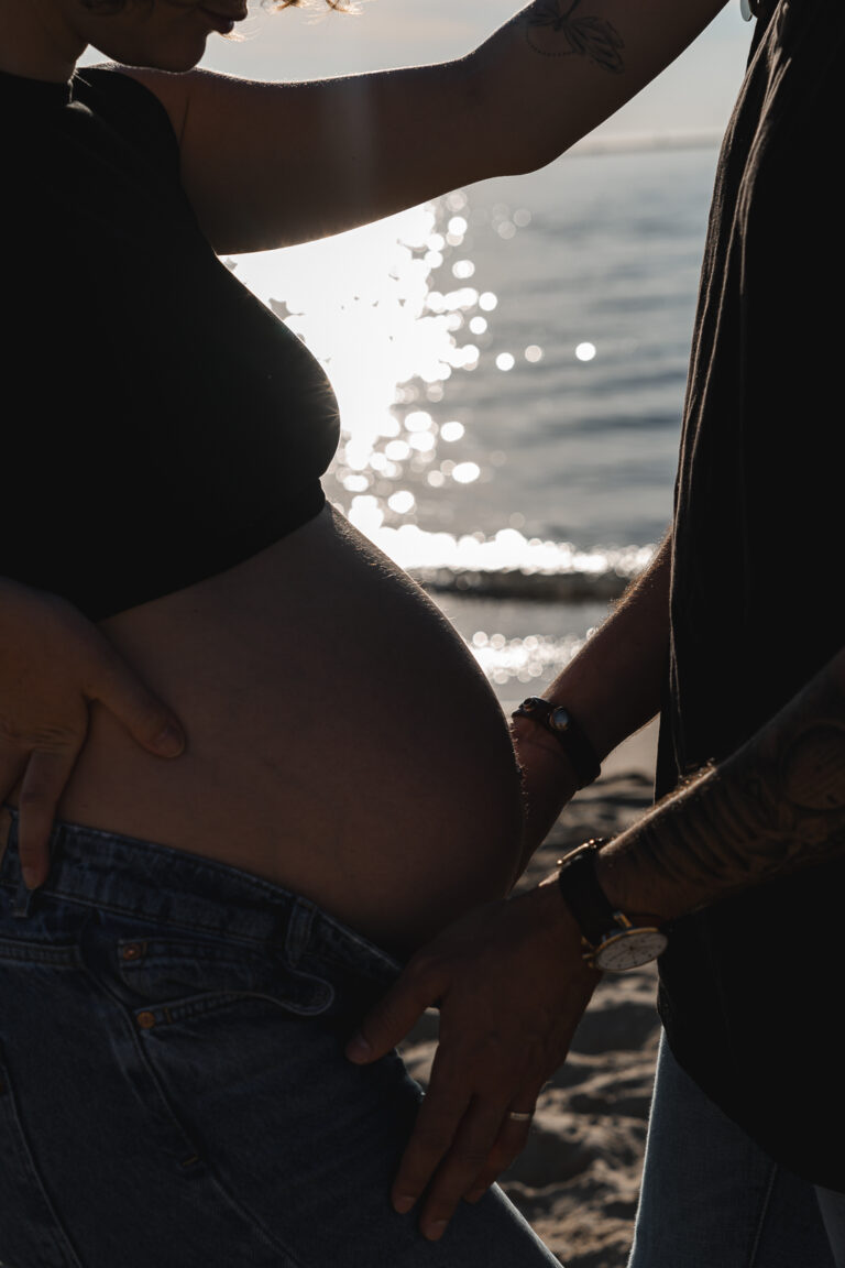 Photo du ventre rond d'une femme enceinte touché par papa lors d'une séance photo grossesse en extérieur à la plage aux dunes du pilat sur le bassin d'Arcachon