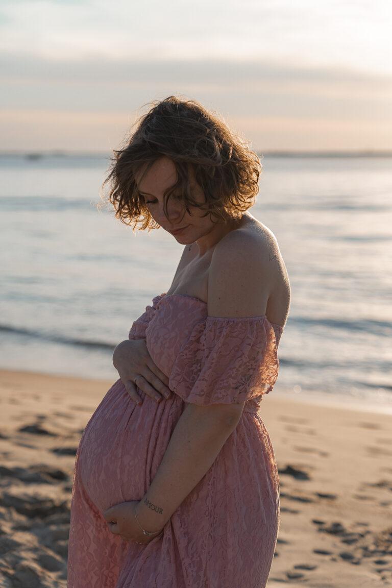 Femme enceinte lors d'une séance photo grossesse en extérieur à la plage aux dunes du pilat sur le Bassin d'Arcachon dans une robe rose prêtée