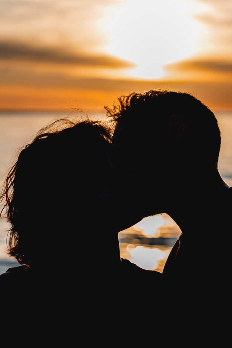 Silhouette d'un couple qui s'embrasse devant un coucher de soleil à la plage de la dune du pilat au bassin d'arcachon pour leurs photos grossesse