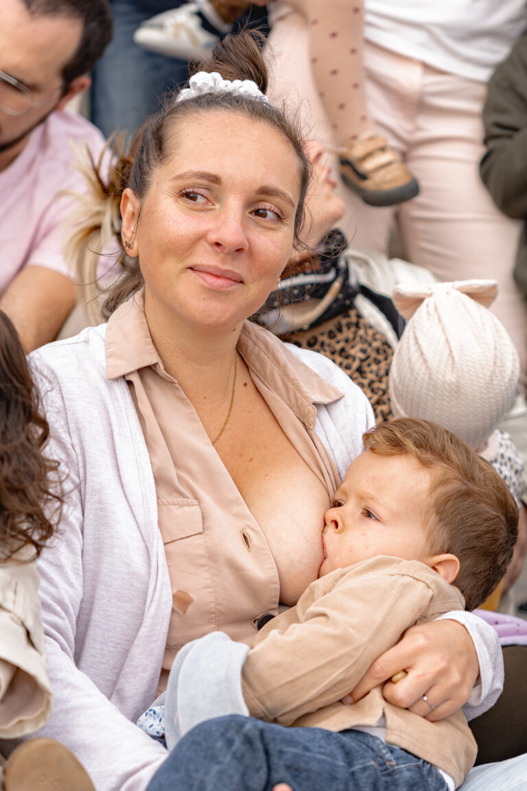 Maman qui allaite son garçon avec un sourire aux lèvres, le regard au loin lors d'une séance photo allaitement en extérieur sur Bordeaux