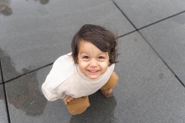 Portrait d'un enfant qui regarde la photographe en souriant sur le miroir d'eau lors d'une séance photo famille en extérieur à Bordeaux