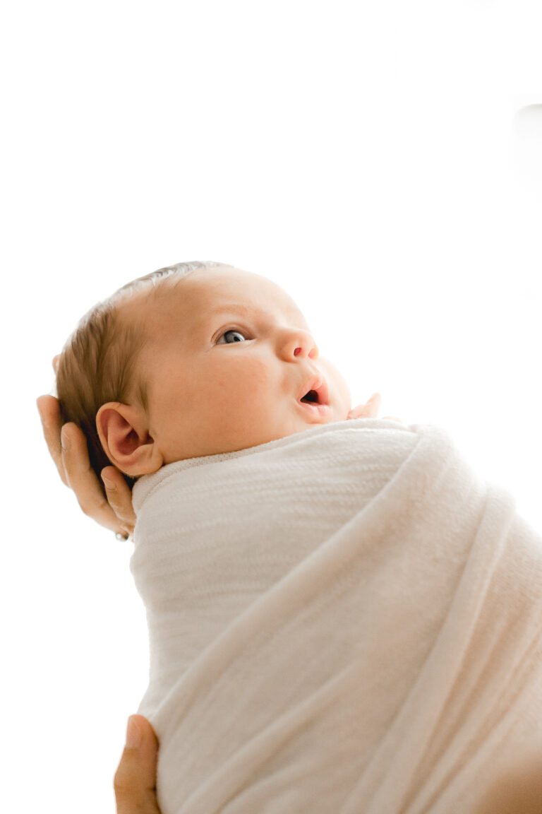 Bébé emmailloté dans un tissu blanc avec une expression mignonne lors d'un shooting bébé à mon home studio sur bordeaux