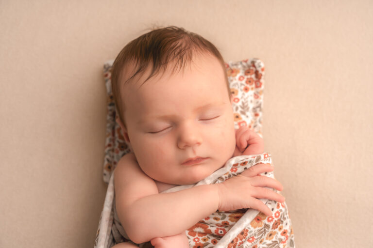 Bébé semi-emmailloté dans un tissu fleuri lors d'une séance nouveau-né à mon home studio sur bordeaux