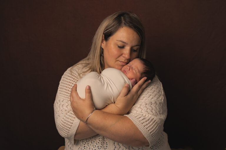 Nouveau-né emmailloté dans les bras de sa maman lors d'une séance photo de naissance à mon home studio sur Bordeaux