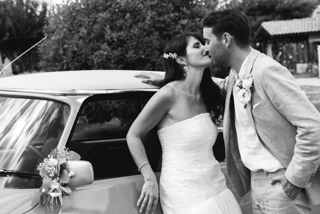 Mariés qui s'embrassent adossés à une voiture de collection lors de la séance couple de leur mariage civil à Salleboeuf