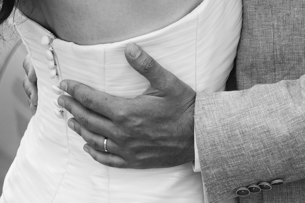 Photo en noir et blanc du détails de la main d'un mari sur la taille de sa femme lors de la séance couple de leur mariage civil à Salleboeuf