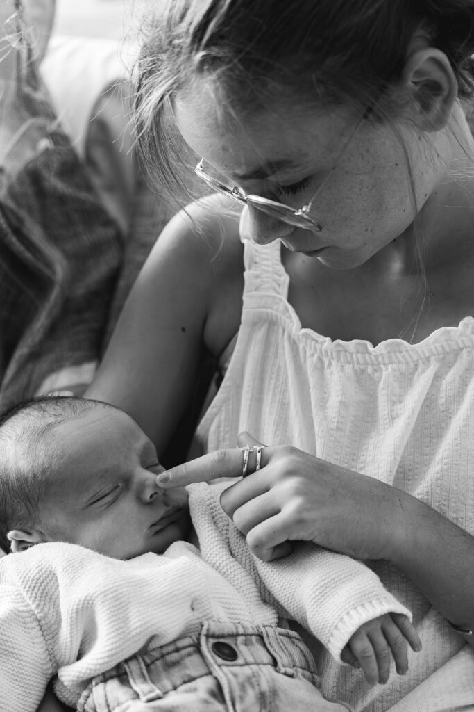 Jeune fille qui tient son petit frère dans les bras et touche son nez du bout du doigt lors d'une séance photo famille à domicile à Mios sur le bassin d'Arcachon