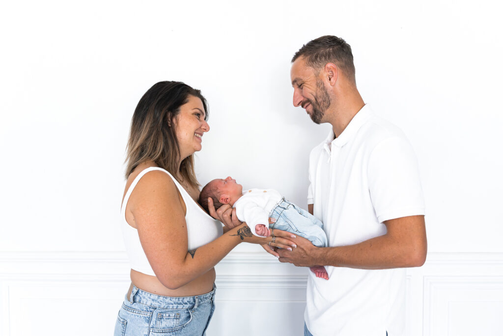 Parents qui sourient face à leur bébé qu'ils tiennent lors d'une séance naissance à domicile à mios sur le bassin d'arcachon