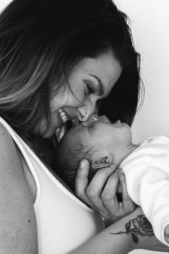 Photo en noir et blanc d'une Maman qui rit nez contre nez avec son bébé qui baille lors d'une séance photo de naissance à domicile à Mios sur le bassin d'arcachon