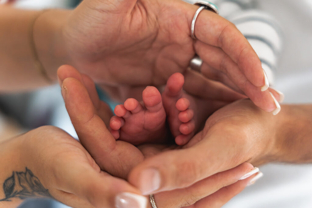 Détails des pieds d'un nourrisson entourés des mains de ses parents lors d'une séance naissance à domicile à Mios sur le bassin d'Arcachon