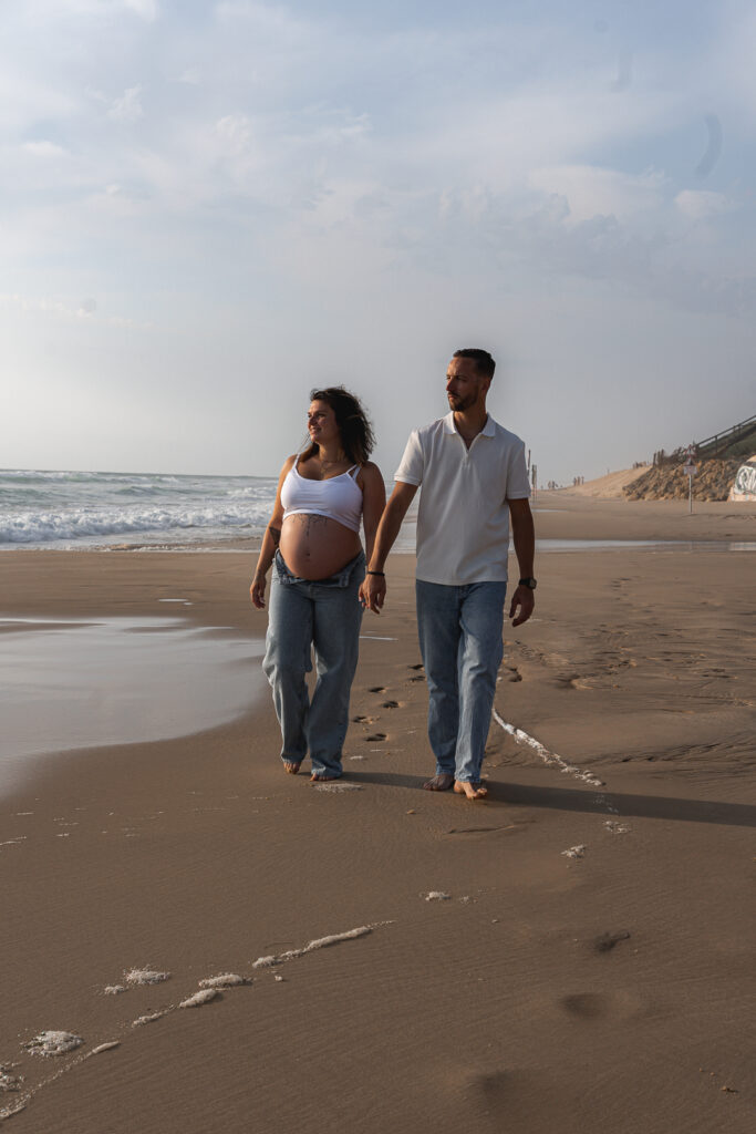Futurs parents se promenant main dans la main au bord de la mer lors de leur séance grossesse à la plage de Biscarosse sur le Bassin d'Arcachon