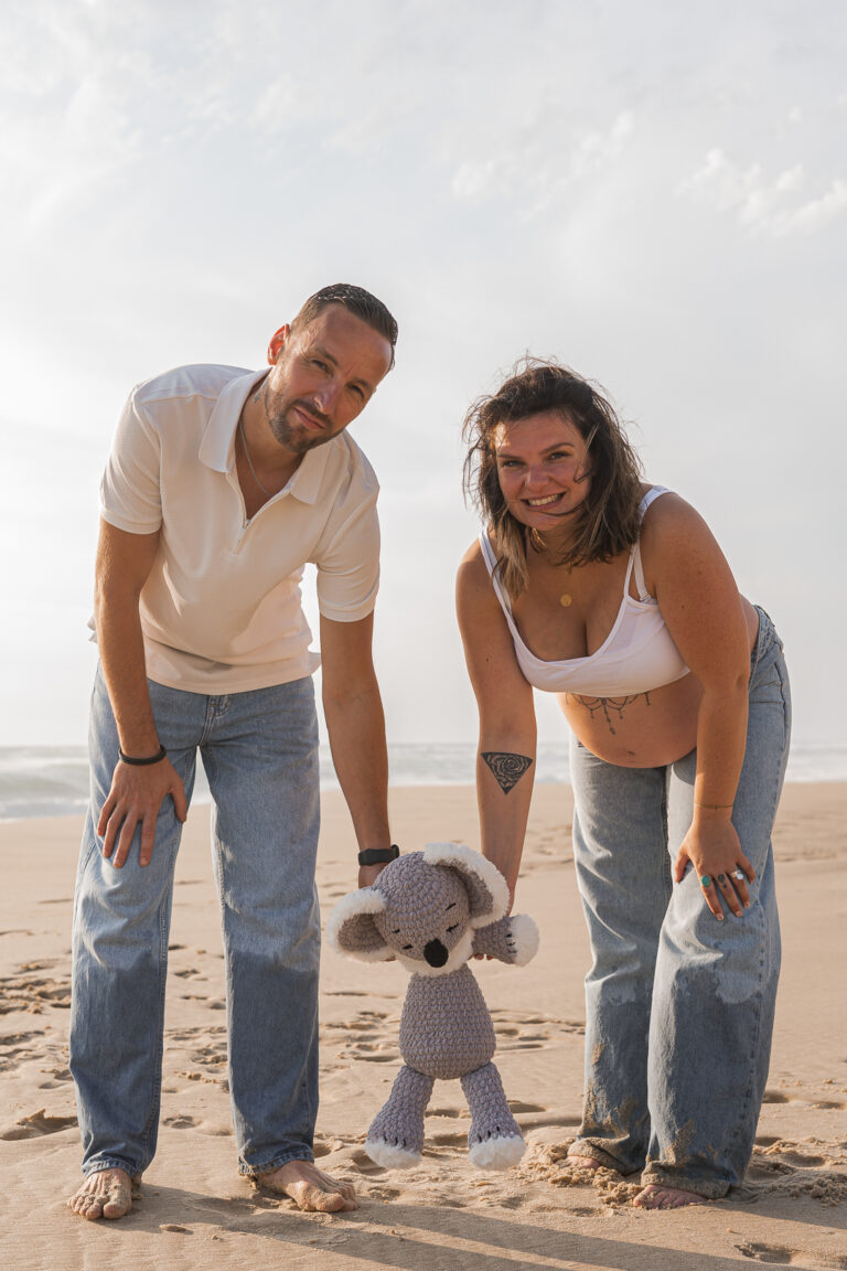 Futurs parents tenant la peluche de leur futur bébé par la main lors de leur shooting grossesse à la plage de Biscarosse sur le bassin d'Archachon