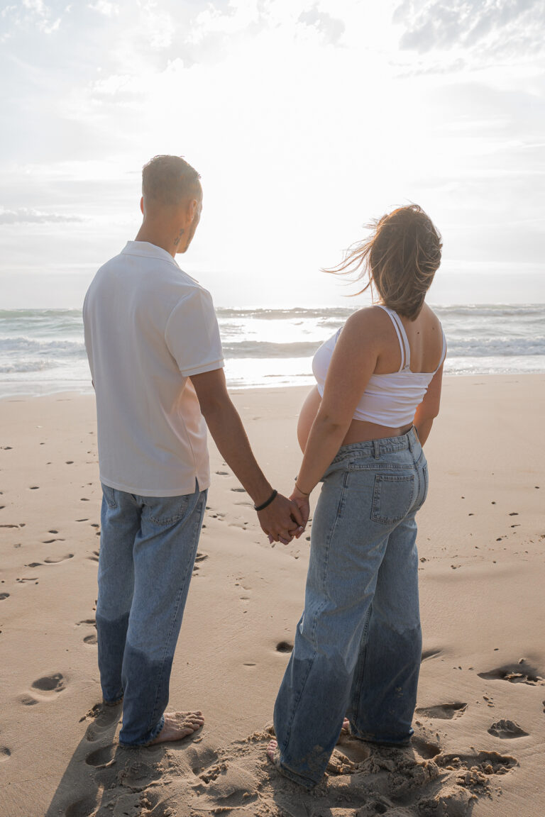 Futurs parents qui regardent le coucher de soleil à la plage de Biscarosse sur le Bassin d'Arcachon lors de leur séance photo grossesse