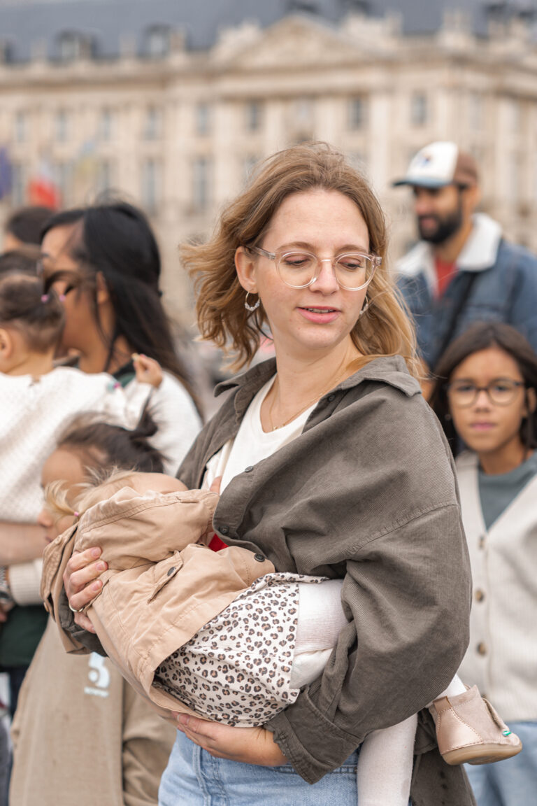 Maman qui allaite sa fille debout en la tenant dans le bras au miroir d'eau de Bordeaux