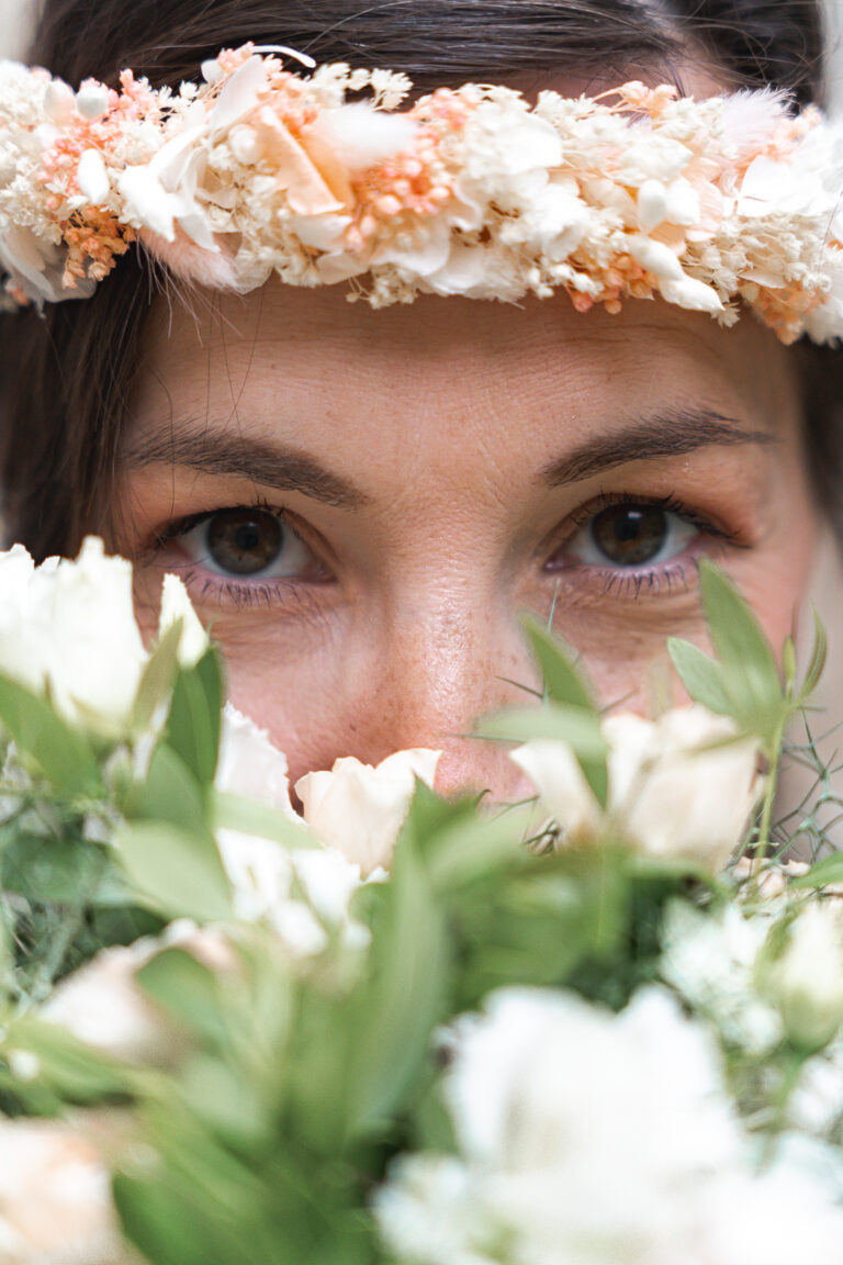 Yeux d'une femme qui se cache derrière un bouquet et porte une couronne de fleurs à la maison Mandel de Bordeaux