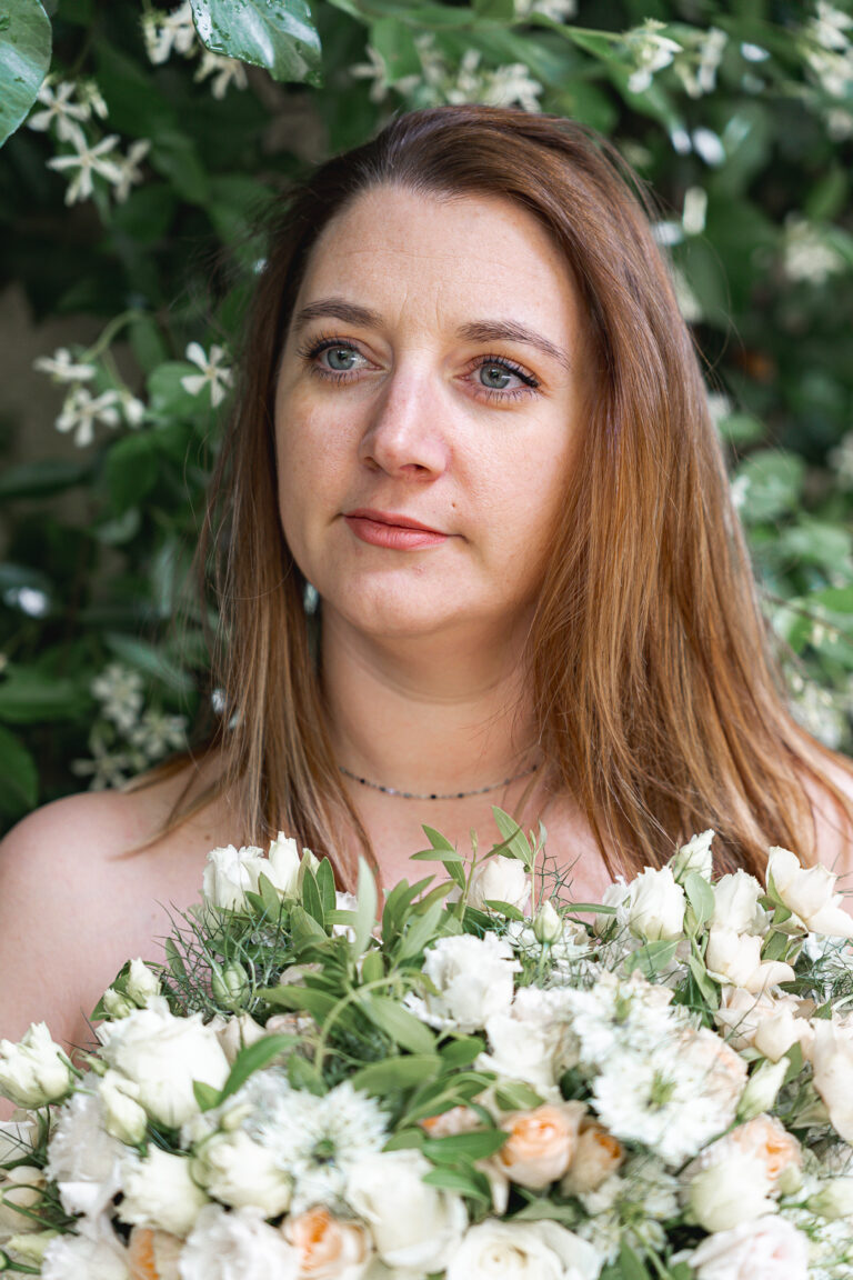 Femme qui pose seins nus cachés par un bouquet de fleurs devant un mur de lierre à la maison Mandel de Bordeaux