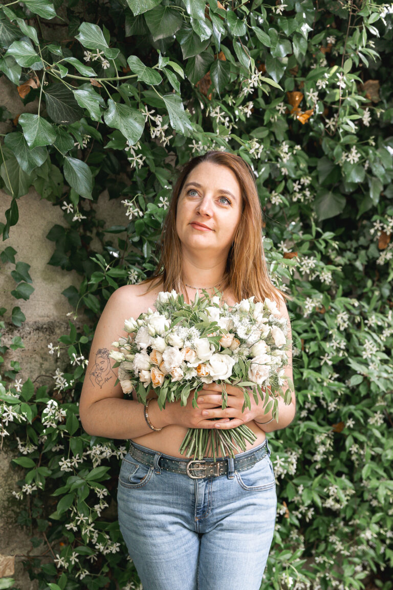 Femme seulement vêtue d'un jean qui regarde le ciel devant un mur de lierre, un bouquet à la main à la maison Mandel de Bordeaux