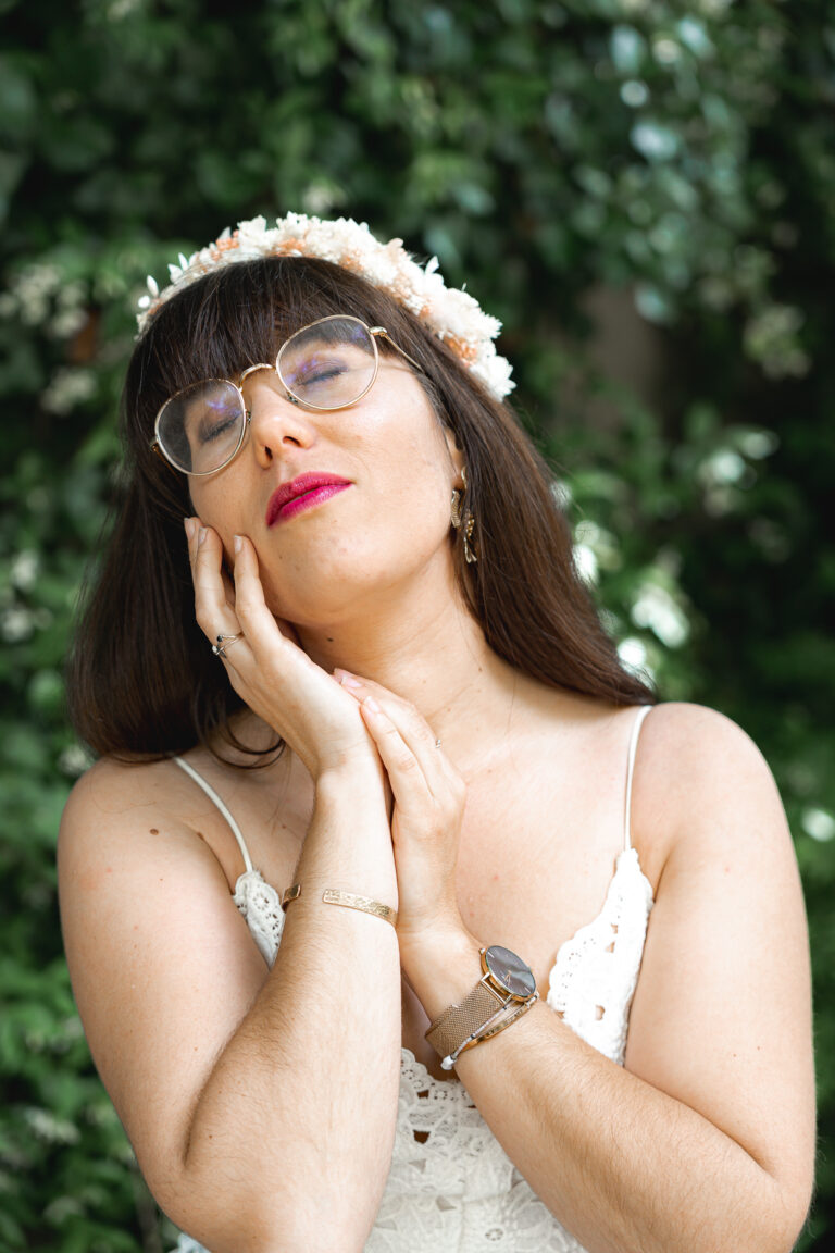 Photographe qui porte une couronne de fleurs en fermant les yeux avec un sourire doux, les paumes l'une contre l'autre à côté de son visage à la maison Mandel de Bordeaux