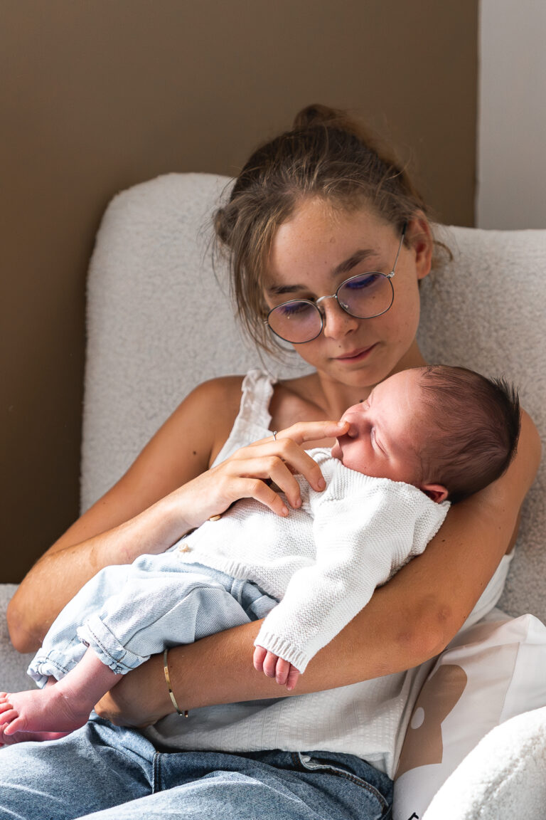 Jeune fille qui touche le nez de son petit frère lors d'une séance photo famille à domicile à mios