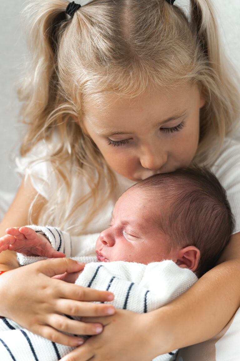 Petite fille qui embrasse son petit frère sur le front lors d'une séance photo en famille à domicile à mios