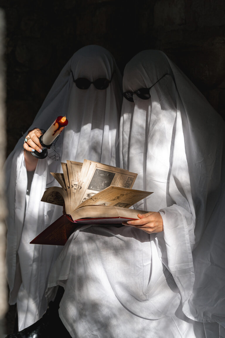 Amis déguisés en fantômes qui lisent un livre de sorcellerie à la bougie lors de leur shooting halloween en extérieur à Blanquefort