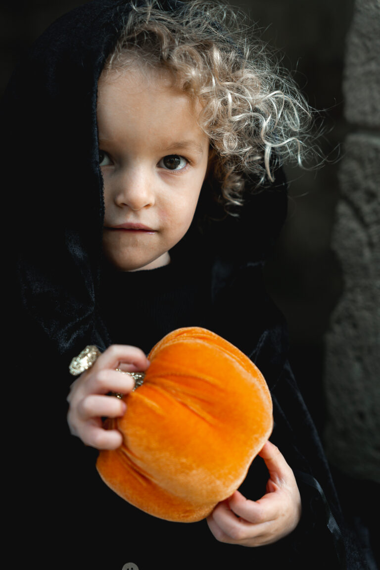 Petite fille avec une cape qui tient une citrouille lors de son shooting halloween en extérieur à Blanquefort
