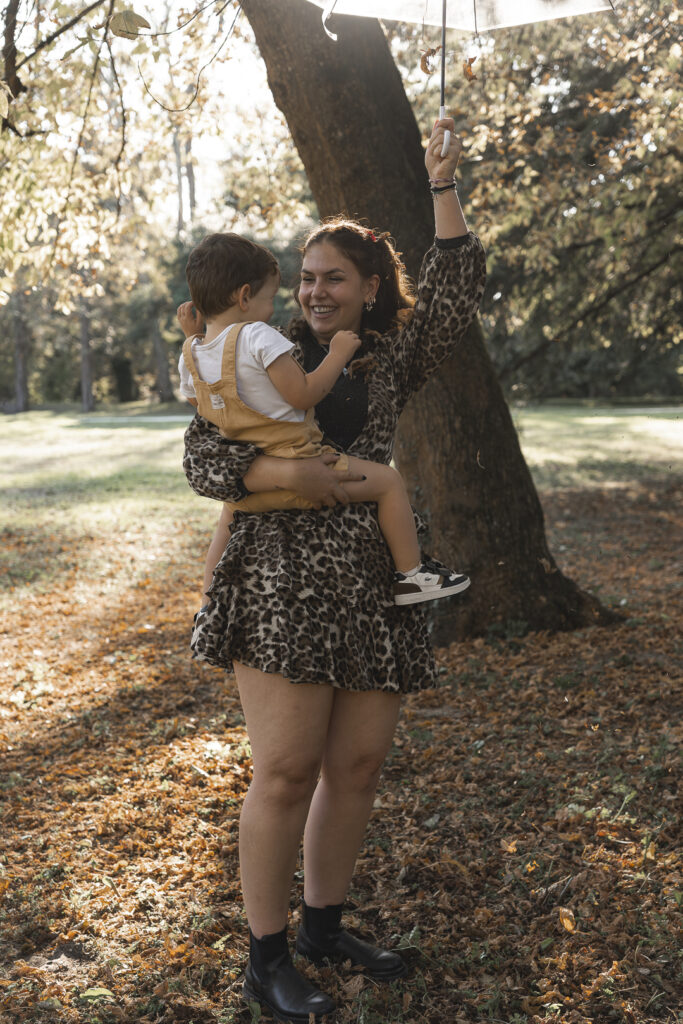 Tante et son neveu debout dans la forêt, renversant un parapluei de feuille au-dessus d'eux pendant un shooting photo famille en extérieur au parc majolan de blanquefort pendant l'automne