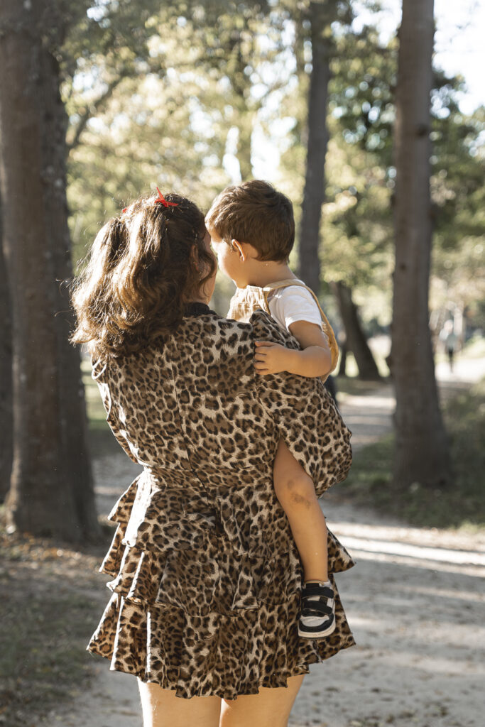 Tante qui marche avec son neveu dans les bras dans une forêt pendant une séance photo famille en extérieur au parc majolan de blanquefort