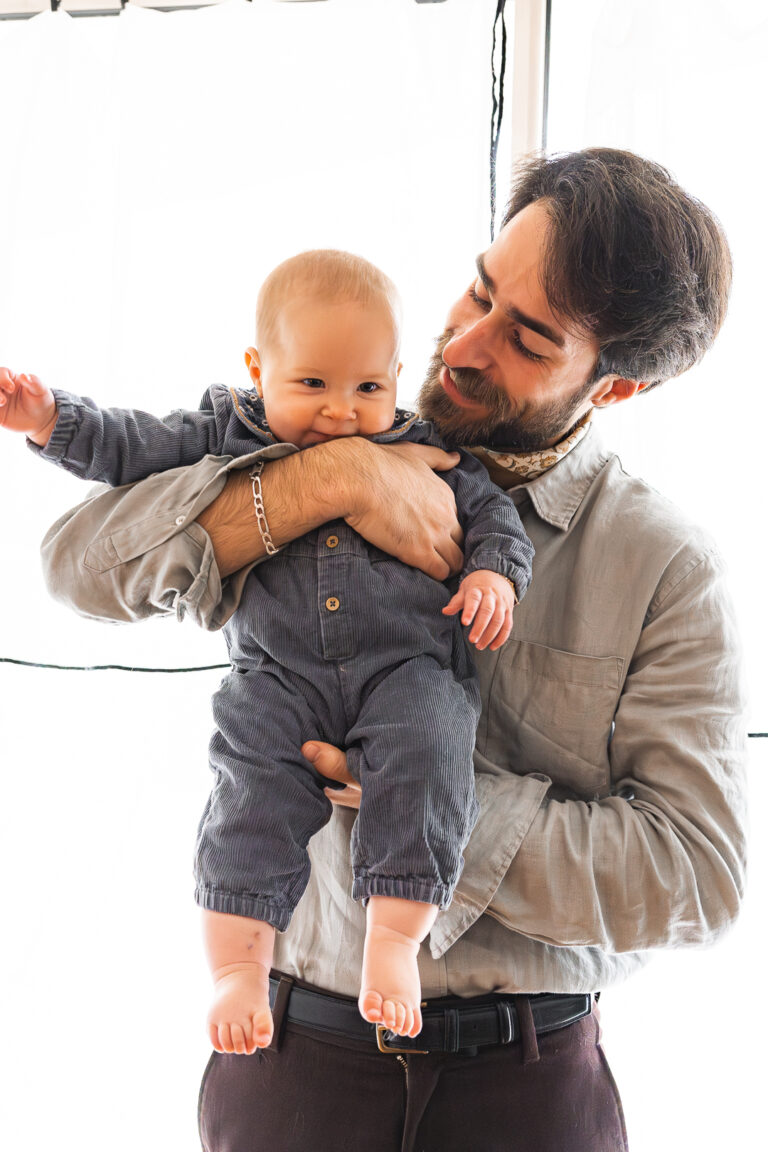 Papa qui tient son bébé dans les bras, face à l'appareil photo lors d'une séance photo fête des pères au home studio à Bordeaux