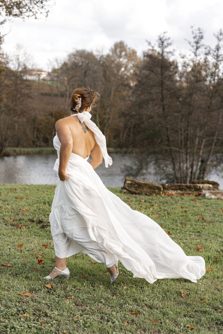 Mariée qui court en regardant derrière elle devant un lac lors du portrait de la mariée de la cérémonie laïque de son mariage au chateau de Courlat à Lussac