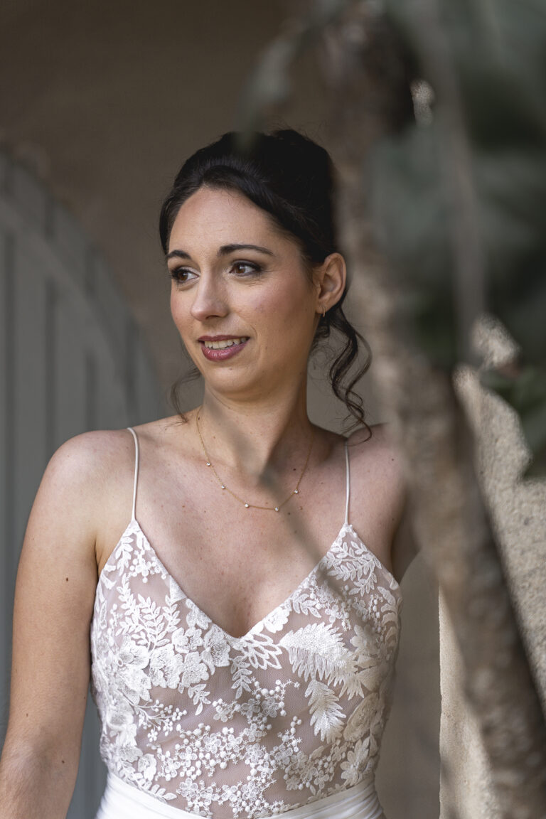 Mariée qui regarde au loin, cachées par des branches lors du portrait de la mariée lors de son mariage au chateau de Courlat à Lussac
