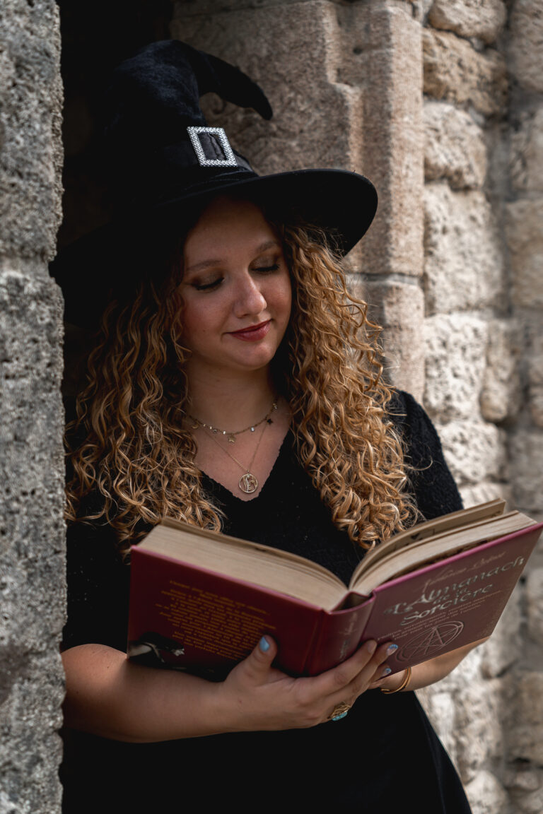 femme déguisée en sorcière qui lit un livre de sorcellerie adossée à un mur lors d'une séance photo halloween en extérieur au parc majolan de blanquefort