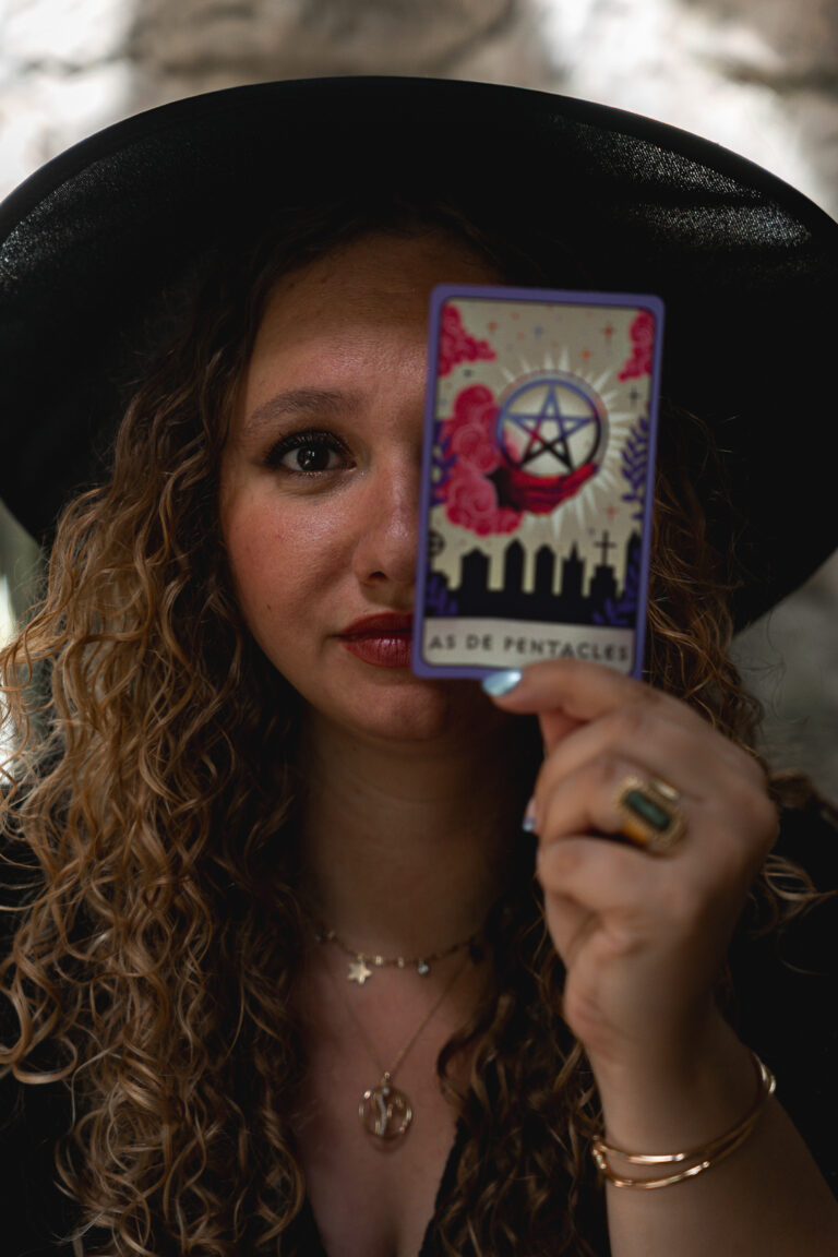 Femme qui tient une carte de tarot devant le côté droit de son visage lors de son shooting halloween en extérieur au parc majolan de Blanquefort