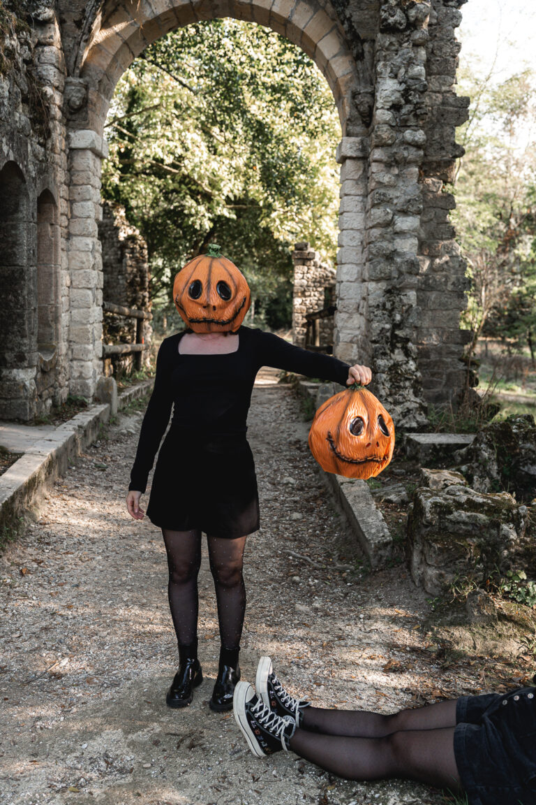 Femme citrouille qui tient une tête de citrouille comme si elle venait de la tuer devant les ruines du parc majolan de blanquefort pendant un shooting halloween en extérieur