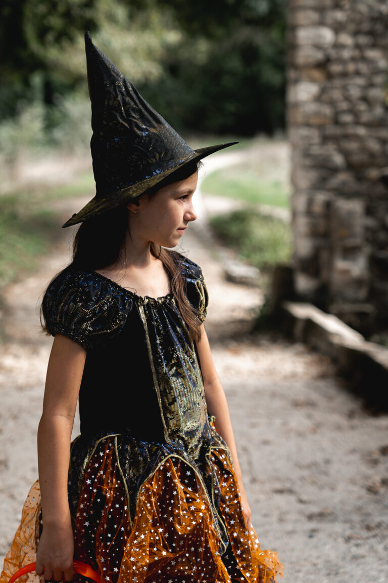 Enfant déguisée en sorcière qui regarde au loin près des ruines du parc majolan de blanquefort lors d'un shooting halloween en extérieur
