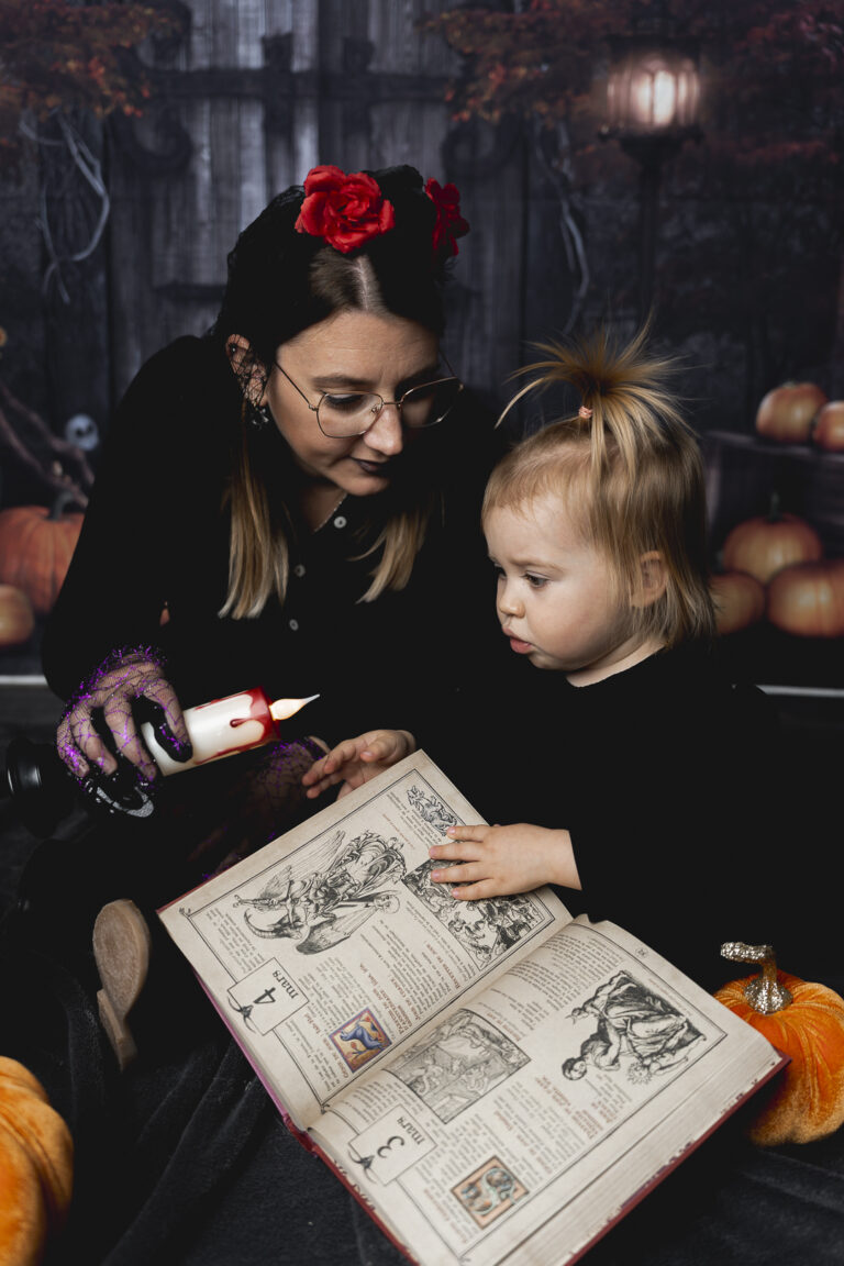 Enfant qui regarde un livre de sorcellerie avec sa maman qui l'éclaire à la bougie lors de leur shooting halloween au home studio à Bordeaux