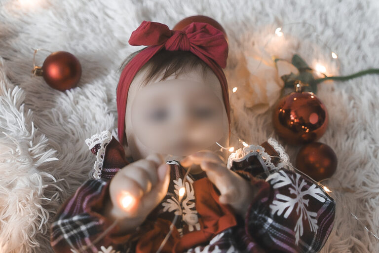 Bébé qui joue avec des guirlandes lumineuses avec une tenue de noël lors d'un shooting photo noël bordeaux