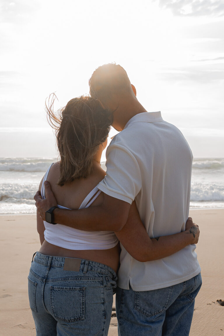 Couple entrelacé qui regarde la mer au coucher du soleil pendant leur séance photo grossesse sur le bassin d'arcachon