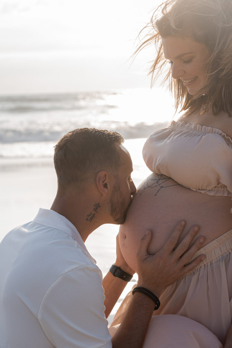 futur papa qui embrasse le ventre d'une future maman devant le coucher du soleil de la plage de biscarosse sur le bassin d'arcachon